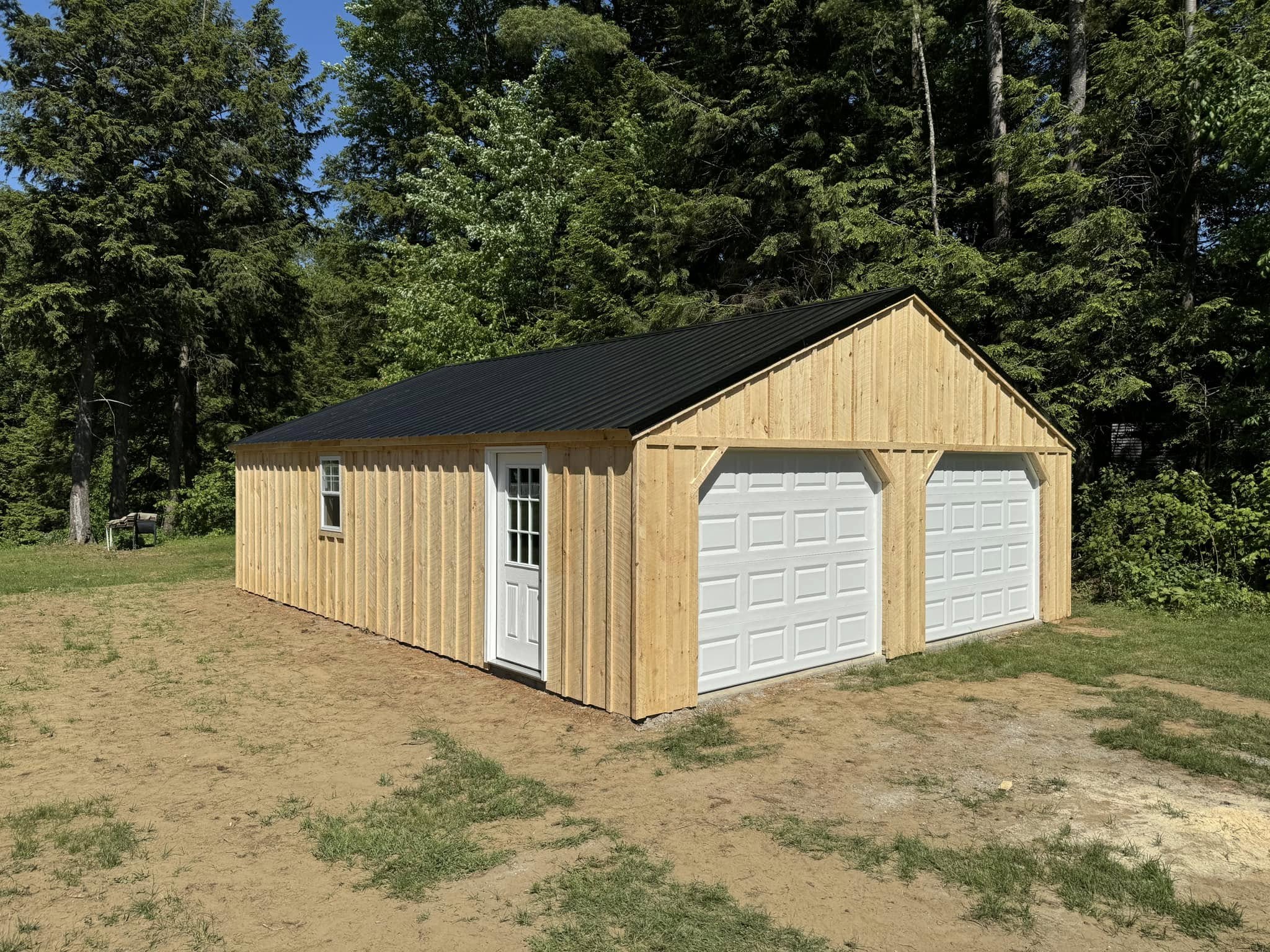 Wood Amish Built Garage with two white garage doors, a white side door, and a black roof